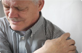 Photo of elderly man rubbing his left shoulder and grimacing.